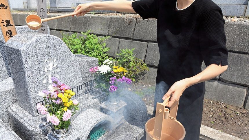 ピアノの形をしたお墓に水をかける女性