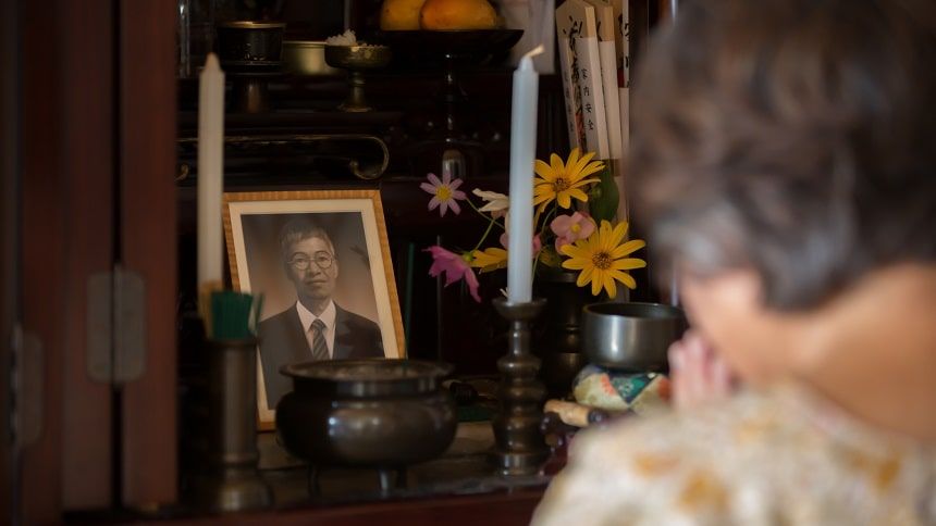 遺影のある仏壇で手を合わせる老婦人